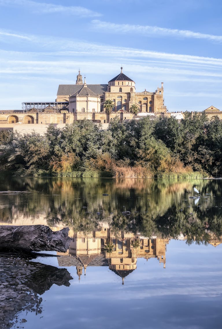 Stunning reflection of the Mosque-Cathedral of Córdoba on the Guadalquivir River, capturing its historic architecture.